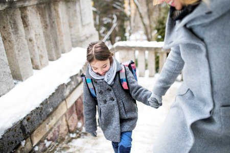 Mother taking daughter to school, saying goodbye in front of the school building, heading to work. Concept of work-life balance for women.の写真素材