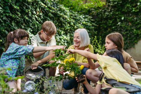 Young kids taking care of plants in school garden during at outdoor sustainable education class, planting flowers, herbs and vegetables. Concept of experiential learning and ecoliteracy.の写真素材