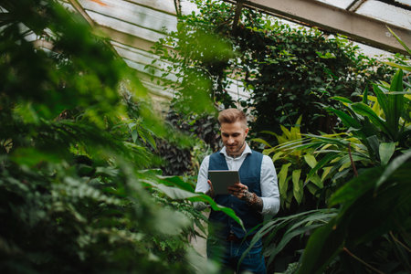 Handsome businessman with tablet, standing in botanical garden, in the middle of lush green foliage. Concept of business corporate social responsibility and ESG.の写真素材