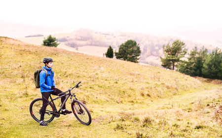 Young man resting by bike in the middle of beautiful nature, early autumn morning. Concept of healthy lifestyle.の写真素材