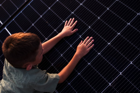 Boy lying on belly on roof with solar panels, touching panel with hands. Rooftop solar or...