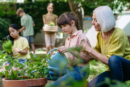 Young kids taking care of plants in school garden during at outdoor sustainable education class,...
