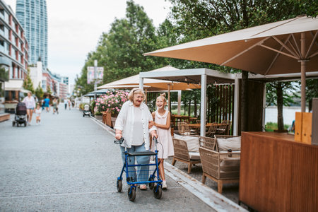 Grandma with walker and granddaugter in the city, on walk. Girl spending time with senior grandmother, during summer break, after school.の写真素材