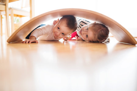 Siblings are playing together in the living room, lying under a wooden arch.