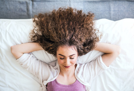 Portrait of beautiful young woman with a curly hair lying on her back on bed. Top view shot.