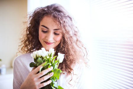 Portrait of beautiful young woman with curly hair looking at bouquet of white roses.の写真素材