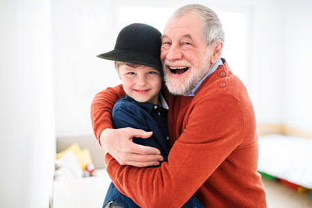 Boy is trying on grandpas big hat, laughing. Grandfather taking care of grandson while parents are at work.の写真素材