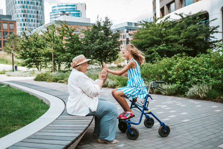Grandma having fun with granddaugter in the city. Girl sitting on walker, spending time with senior grandmother, during summer break, after school.の写真素材