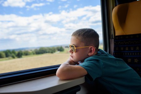 Boy sitting in train, looking out of window and enjoying journey. Family going on hike, using public...