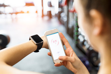 Young fitness girl checking her performance on smatphone and smartwatch after hard workout in gym.の写真素材