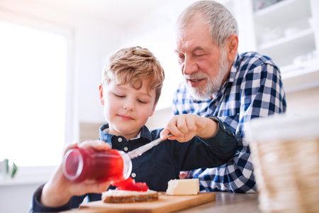 Boy and grandpa making breakfast in the kitchen. Grandfather spending time with grandson, taking care of him while parents are at work.の写真素材