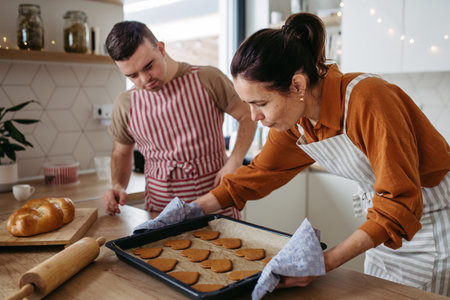 Young man with Down syndrome and his mom baking Christmas gingerbread cookies. Christmas peaceful moment for man with Down syndrome.の写真素材