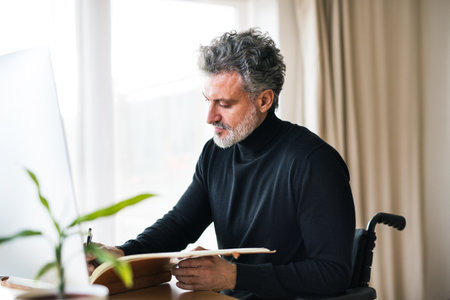 Handsome man in wheelchair working from home office, using computer in office. Telecommuting and home office.の写真素材
