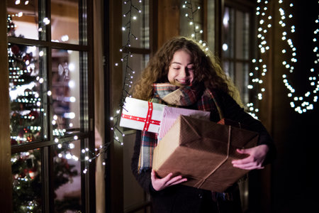 Young woman is shopping for Christmas gifts, carrying a bunch of presents in her hands, walking out...