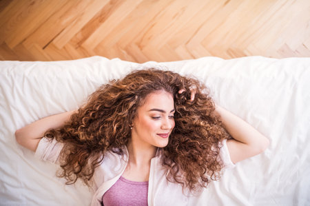 Portrait of beautiful young woman with a curly hair lying on her back on bed. Top view shot.の写真素材