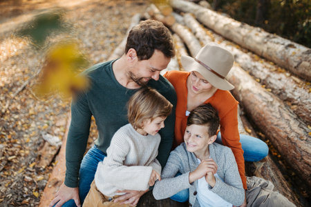 Portrait of family sitting on logs in the middle autumn forest. Nuclear family spending weekend...