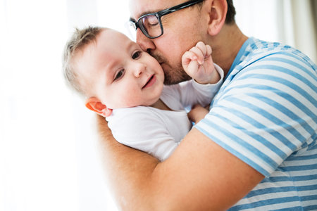 Portrait of father with little son. Dad kissing boy on cheek and hugging him.