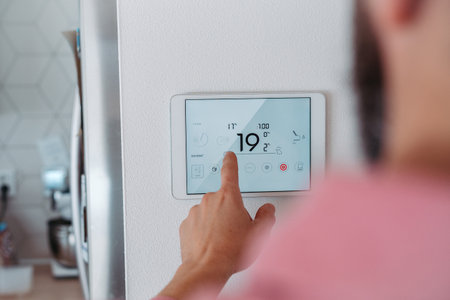 Man using smart thermostat, adjusting, lowering heating temperature at home. Concept of smart...
