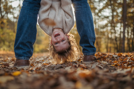 Father holding little girl by legs heand down, playing during walk in autumn forest. Dad and girl...