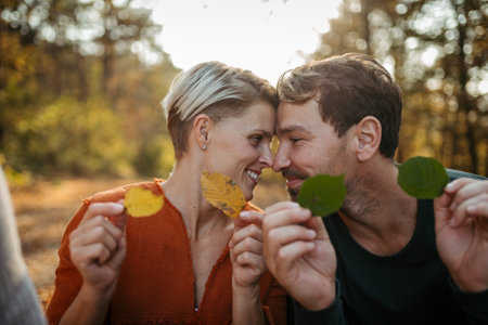 Couple holding colorful leaves, looking at camera. Man and woman on walk in autumn forest.の写真素材