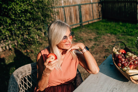 Senior female gardener holding a freshly picked apple from apple tree. Own harvest, gathered in the...