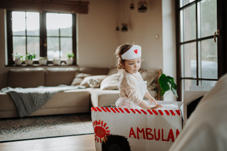 Girl in doctor uniform is playing hospital. Little girl as nurse sitting in cardboard ambulance.の写真素材