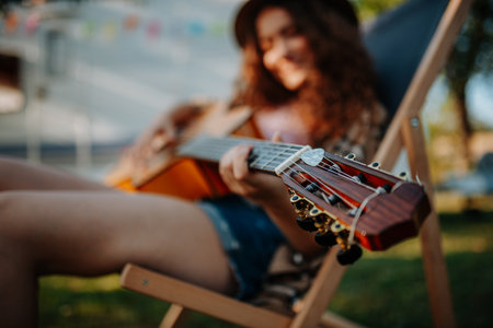 Young beautiful woman is on a camping trip in nature, sitting in front caravan and playing guitar.の写真素材