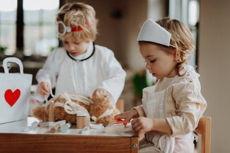 Siblings in doctor uniforms are playing hospital, taking care of sick teddy bear.の写真素材