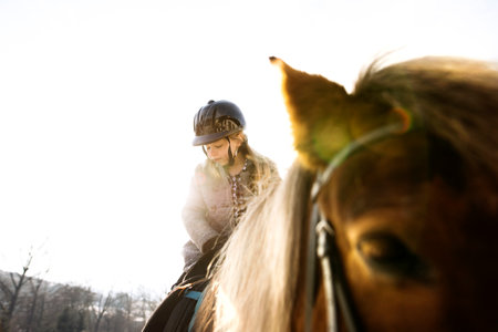 Low angle view of young girl riding her brown fluffy pony. Girl spending cold winter weekend on family farm.の写真素材