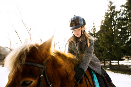 Young girl spending cold winter weekend on family farm, riding her brown fluffy pony through snowy countryside.の写真素材