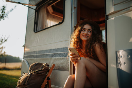 Portrait of young beautiful woman on a camping trip in nature, sitting on caravan steps with...