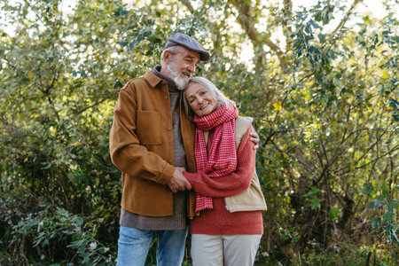 Portrait of beautiful senior couple outdoors in an autumn garden. Elderly husband and wife are embracing each other.の写真素材
