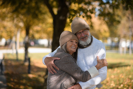 Portrait of beautiful senior couple during walk in autumn park. Elderly husband and wife are embracing each other.の写真素材