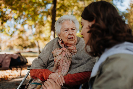 Disabled elderly woman in wheelchair holding hands with her caregiver, talking.の写真素材
