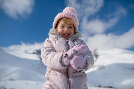 Portrait of small girl enjoying winter holiday in the mountains with family, playing in snow.