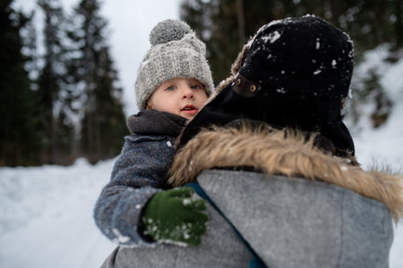 Father standing in the middle of snowy forest holding young son in arms. Dad and boy enjoying winter...