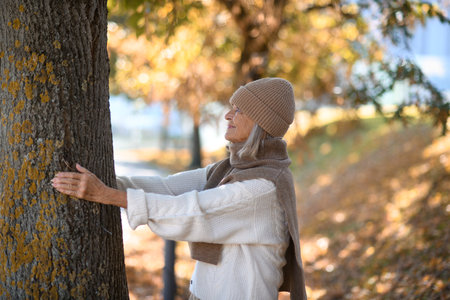 Portrait of a beautiful senior woman hugging tree trunk with closed eyes. Elderly woman in connection with nature.の写真素材
