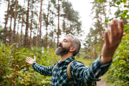 Handsome man standing in the middle of nature with open arms, enjoying peaceful atmosphere of the...