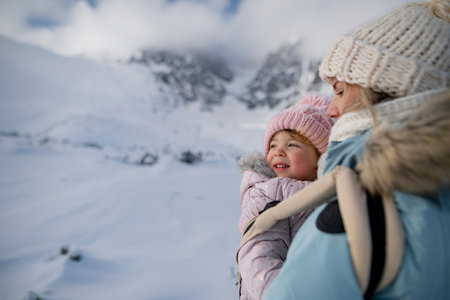 Mother standing in the middle of snowy landscape with daughter in baby carrier. Mom and girl...
