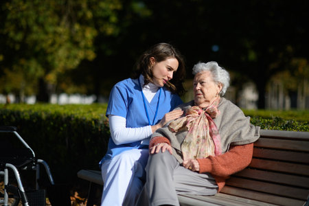 Elderly woman talking with therapist in park, sitting on bench. Outdoor therapy for senior woman in nursing home.の写真素材