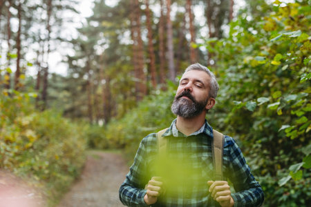 Handsome man standing in the middle of nature with closed eyes, enjoying peaceful atmosphere of the forest, forestbathing.の写真素材