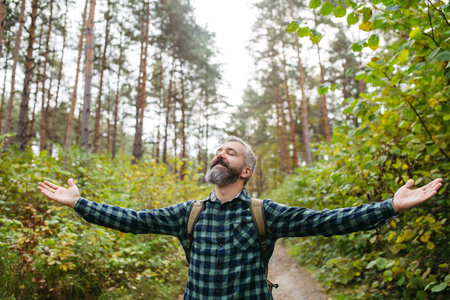Handsome man standing in the middle of nature with open arms and closed eyes. Peaceful atmosphere of the forest, forestbathing.の写真素材
