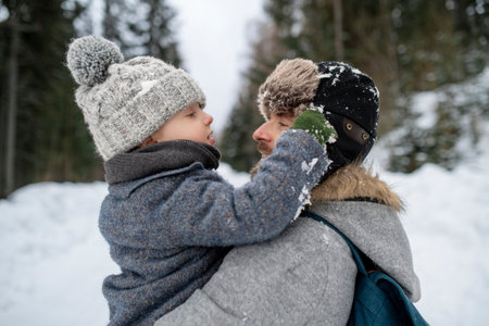 Father standing in the middle of snowy forest holding young son in arms. Dad and boy enjoying winter holiday in the mountains.の写真素材