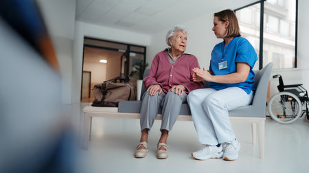 Hospital nurse delivering bed news to family member of patient. Old patient sitting in hospital corridor suffering from pain.の写真素材