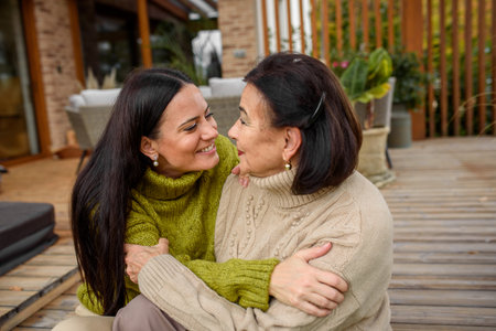 Mature daughter with older mom sitting on wooden patio, hugging. Mothers day concept.の写真素材