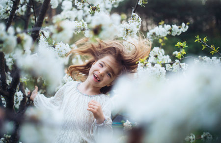 Laughing young girl dancing in the middle of blooming flowers. Concept of springtime in nature.の写真素材