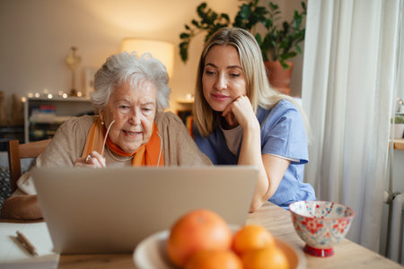 Elderly woman learning how to work with laptop, social worker helping her. Managing finances and...