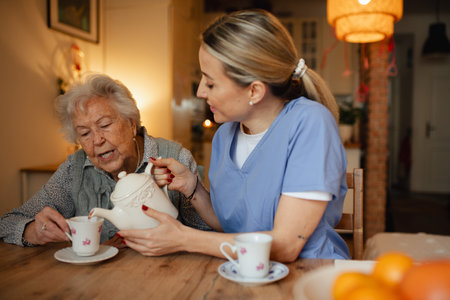 Lovely eldery woman serving tea to friendly caregiver.の写真素材