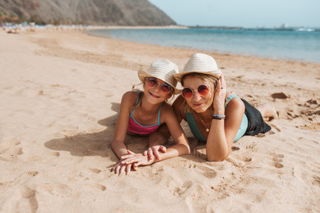 Portrait of mother and daughter lying on a sandy beach, wearing hats and sunglasses.の写真素材