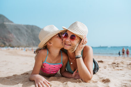 Portrait of mother and daughter on a sandy beach, wearing hats and sunglasses.の写真素材